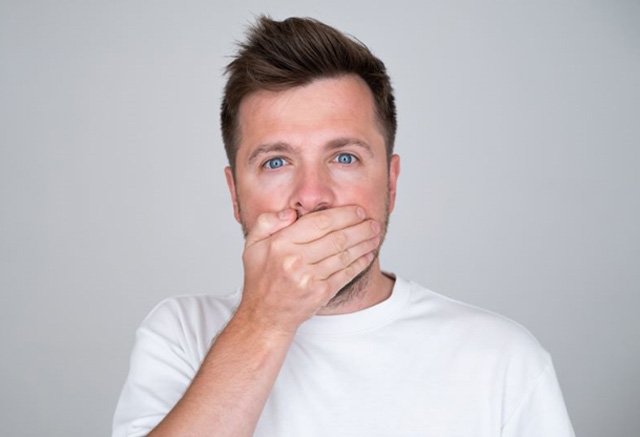 Concerned man in white t-shirt covering his mouth