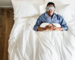 Man in bed, wearing pajamas and eye mask