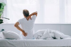 Man sitting on bed, struggling with aches and pains